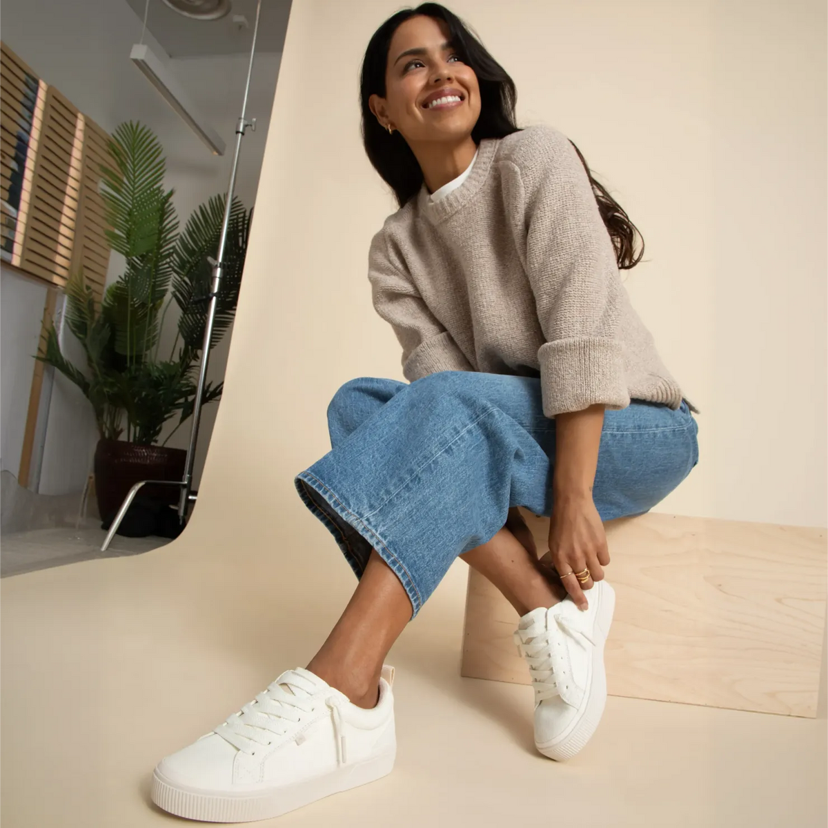 Woman wearing Lay Day Dawn white suede sneakers facing left, seated with a smile, showcasing comfort and casual style