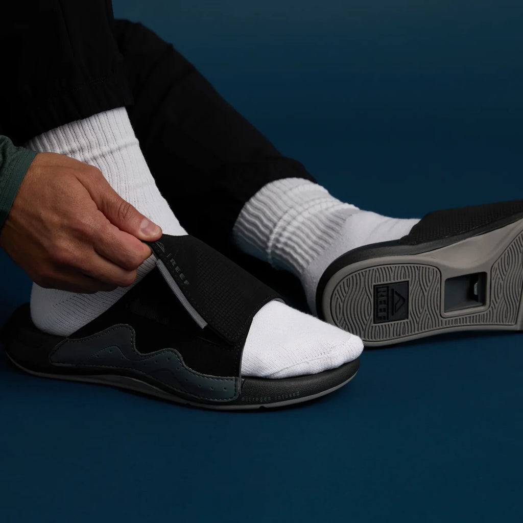 Black Cruiser Slide facing left with white socks, shown from side and bottom highlighting cushioning and arch support.