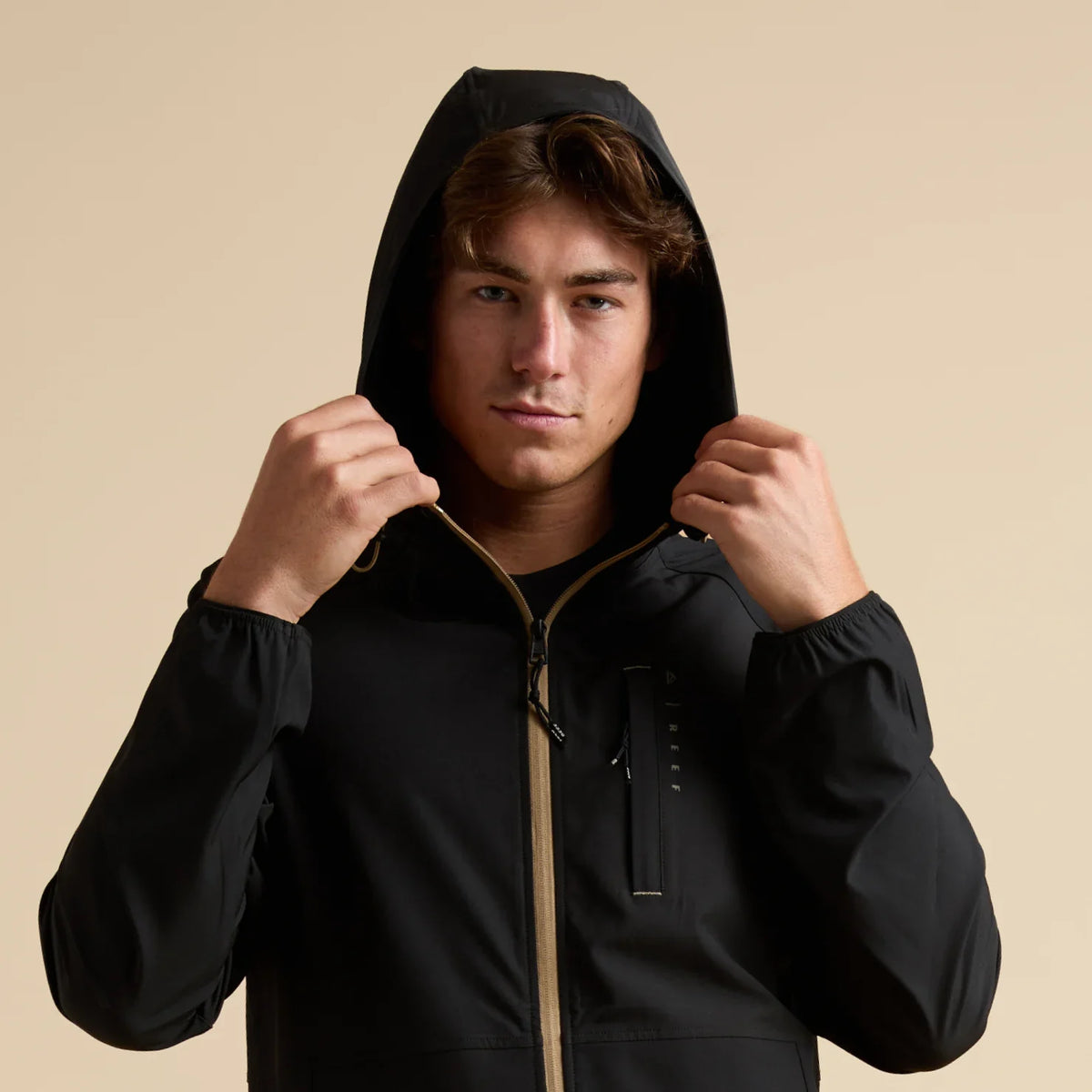 Man wearing a black Garvey Full Zip Jacket with hood up, front view showing front zipper and chest pocket details.