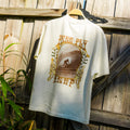 Back view of High-Stoke Relaxed Tee - Bone hanging outdoors showing surf-inspired graphic with beach lifestyle vibe