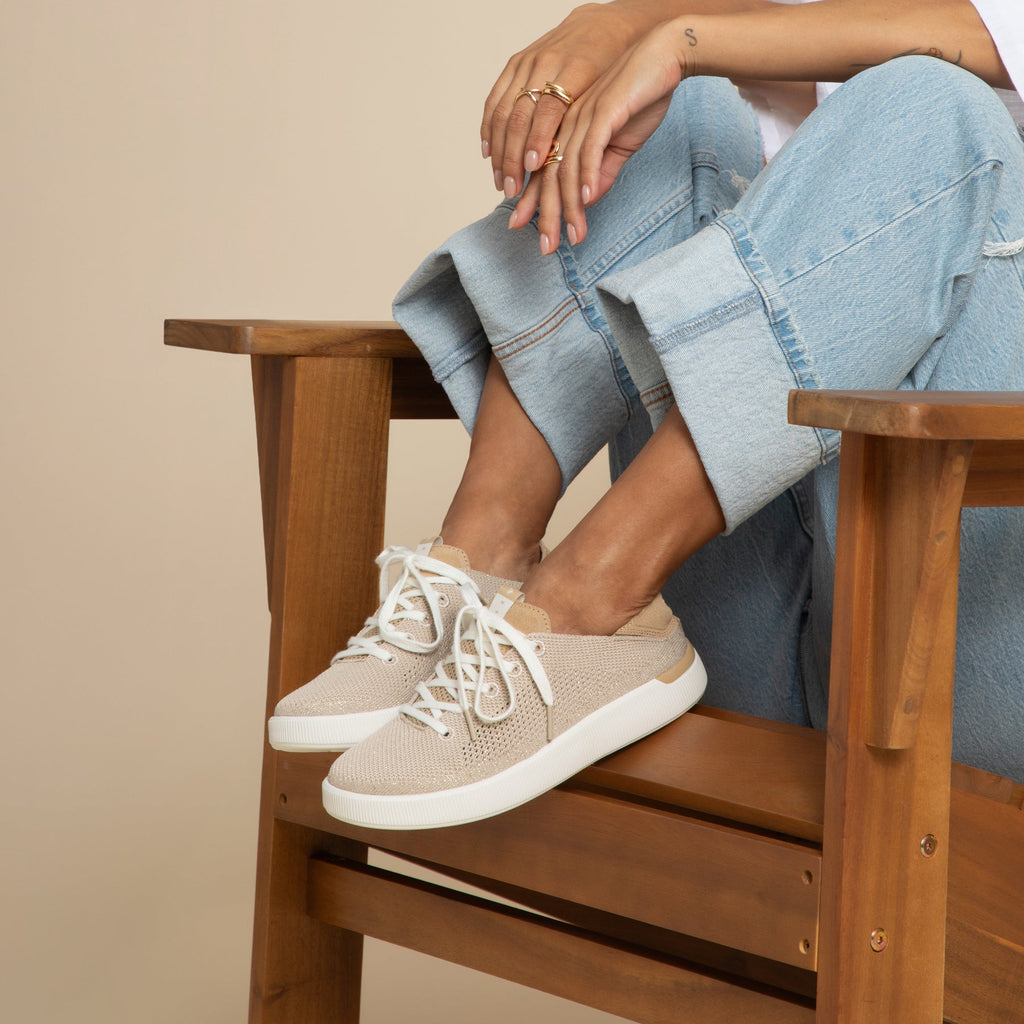 Reef Neptune womens beige slip-on sneaker facing right with soft cushioning and arch support, worn seated in wooden chair.