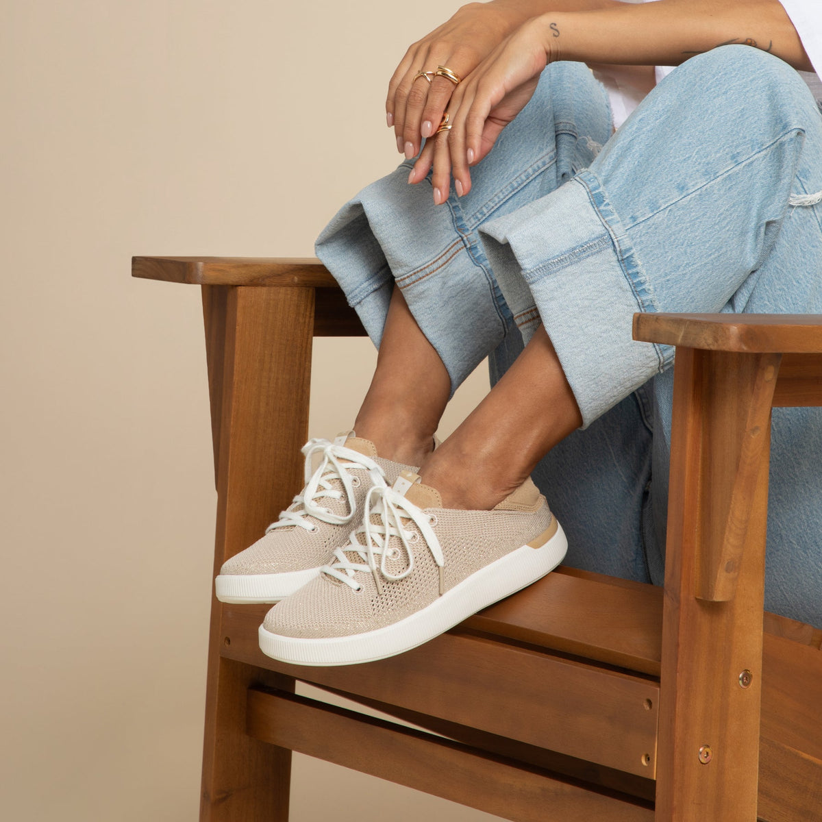 Reef Neptune womens beige slip-on sneaker facing right with soft cushioning and arch support, worn seated in wooden chair.
