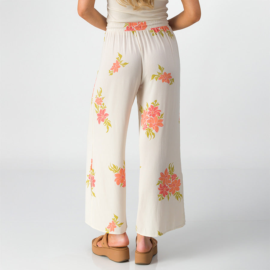 Woman wearing Belladona Pant with floral print, shown from back, paired with tan platform sandals facing backward.