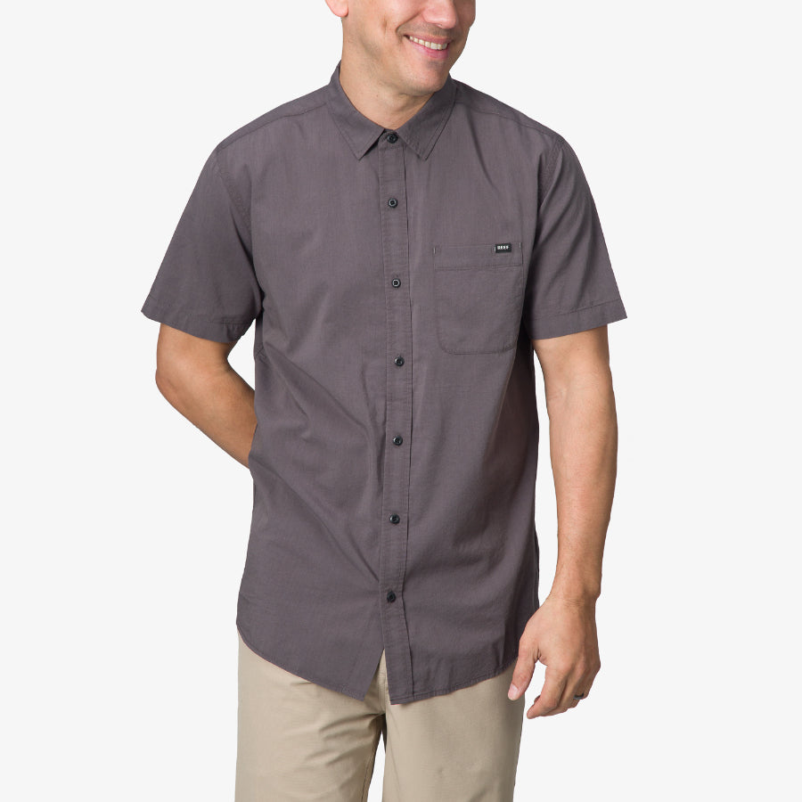 Man wearing a grey Collins Ss Wvn Shirt with button front and chest pocket, front view, casual beach-inspired apparel.