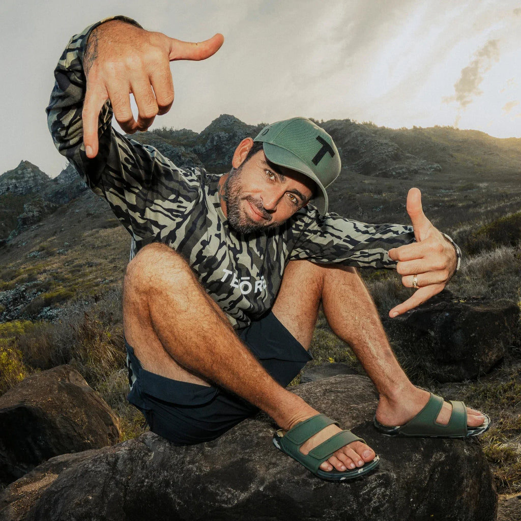 Man sitting outdoors wearing green Oasis Adapt sandals facing forward, showcasing comfort and beach-inspired style.