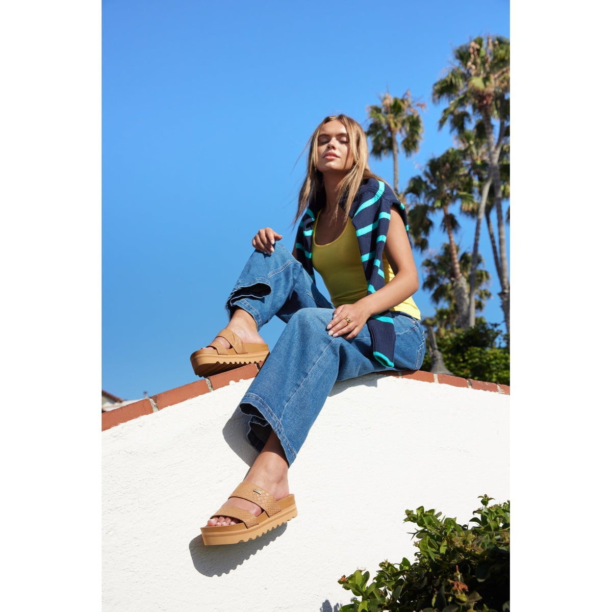 Woman sitting outdoors wearing tan Cushion Vista Hi sandals facing left with arch support and soft cushioning visible