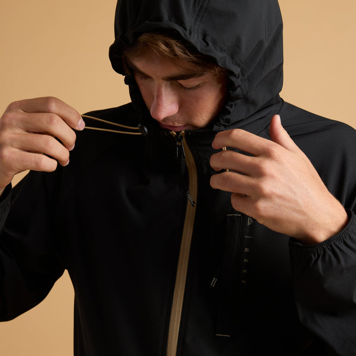 Man adjusting hood strings on black Garvey Full Zip Jacket, close-up of front zipper and lightweight fabric details.