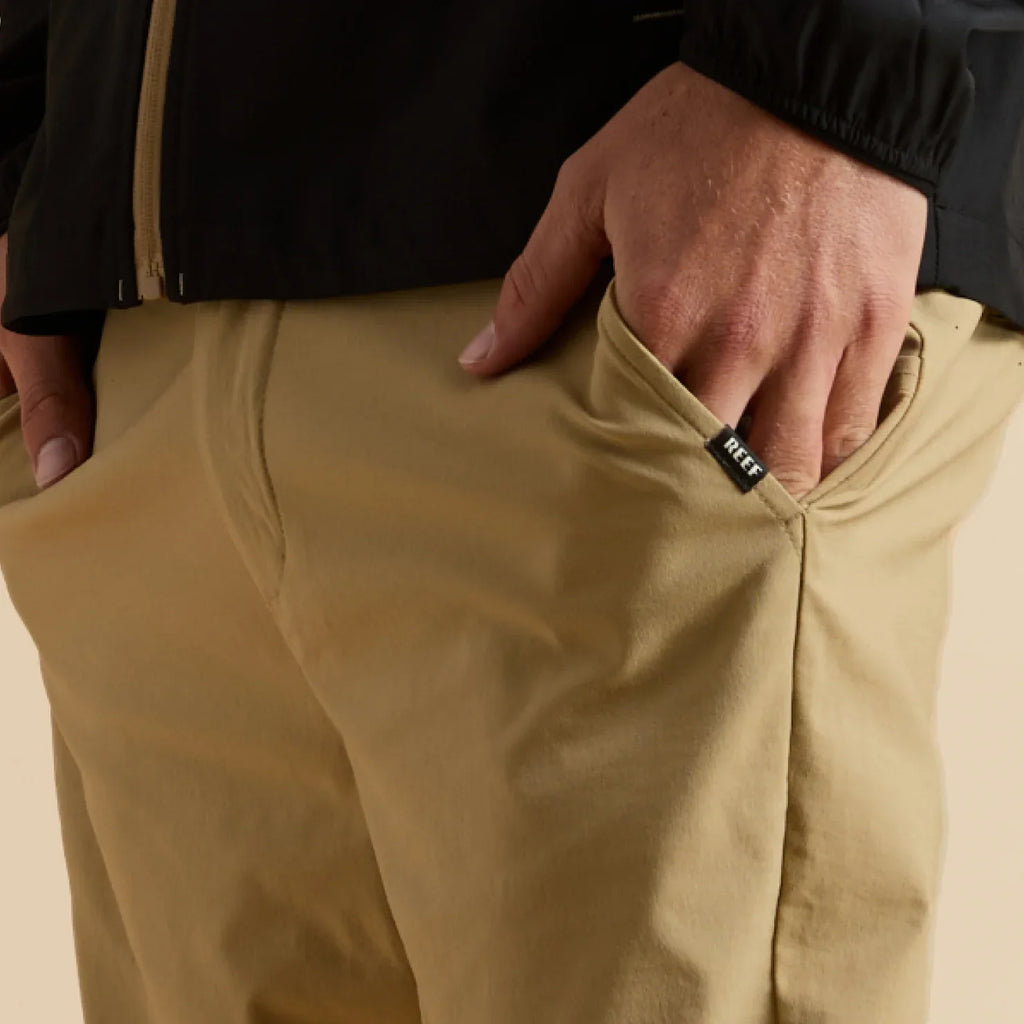 Close-up of a man's hand in the front pocket of tan Carrick Stretch Pant, showcasing comfort and stretch fabric.