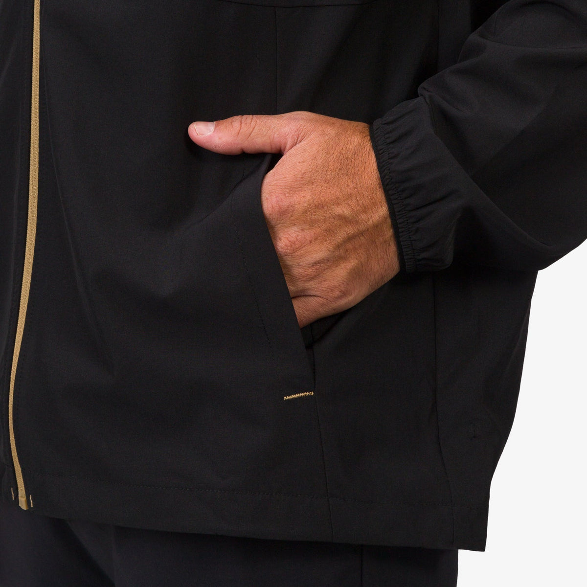 Close-up of a man's right hand in the side pocket of a black Garvey Full Zip Jacket showing fabric and cuff details.