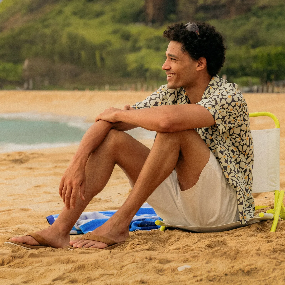 Man wearing Nox sandals facing left, sitting on sandy beach with surf-inspired comfort and arch support features.