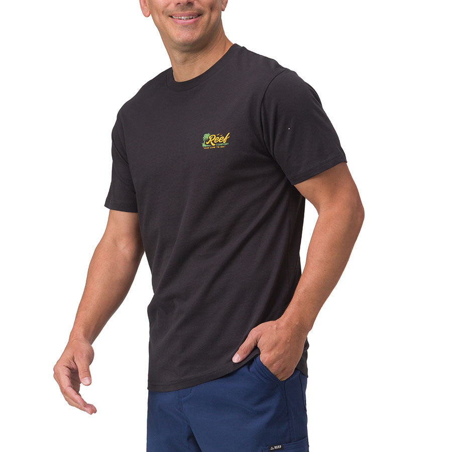 Man wearing black Isac Tee with small yellow Reef logo on chest, hands by sides, standing in relaxed pose