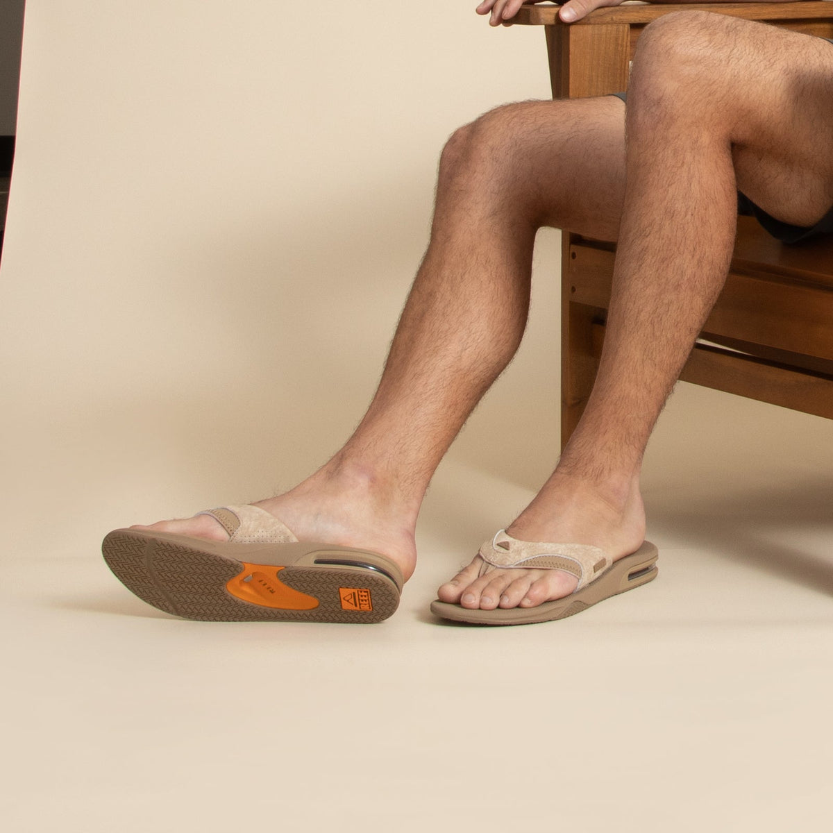 Fanning men's tan flip flop facing left with close-up on footbed and soft-rebound cushioning, surf-inspired comfort.